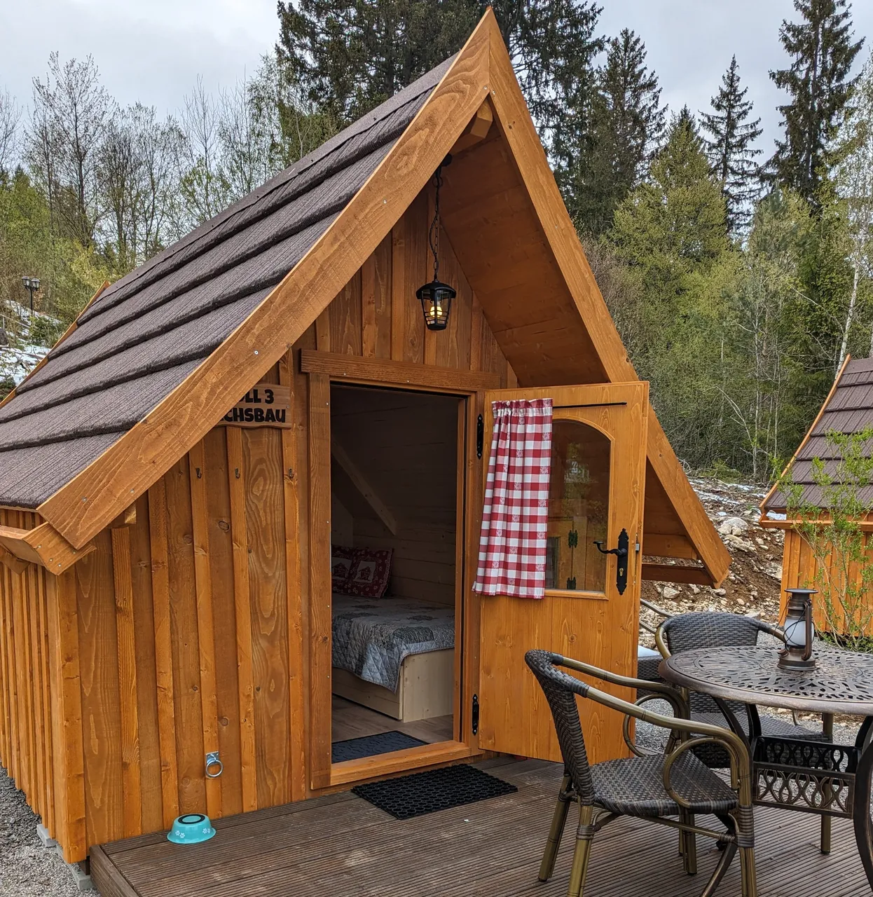 Kleine Holz-Ferienhütte mit Terrasse und geöffneter Tür im Wald