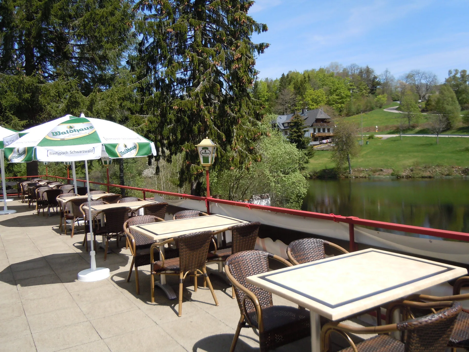 Sonnige Seeblickterrasse mit Tischen, Sonnenschirmen und Blick auf den Klosterweiher